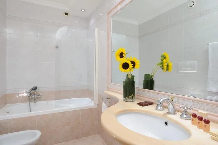 Representative hotel space: A bright tiled bathroom with a bathtub, sink, and sunflower arrangement.