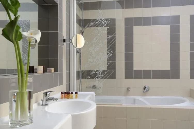 Representative hotel space: A tiled bathroom with a bathtub, sink, and a potted flower.