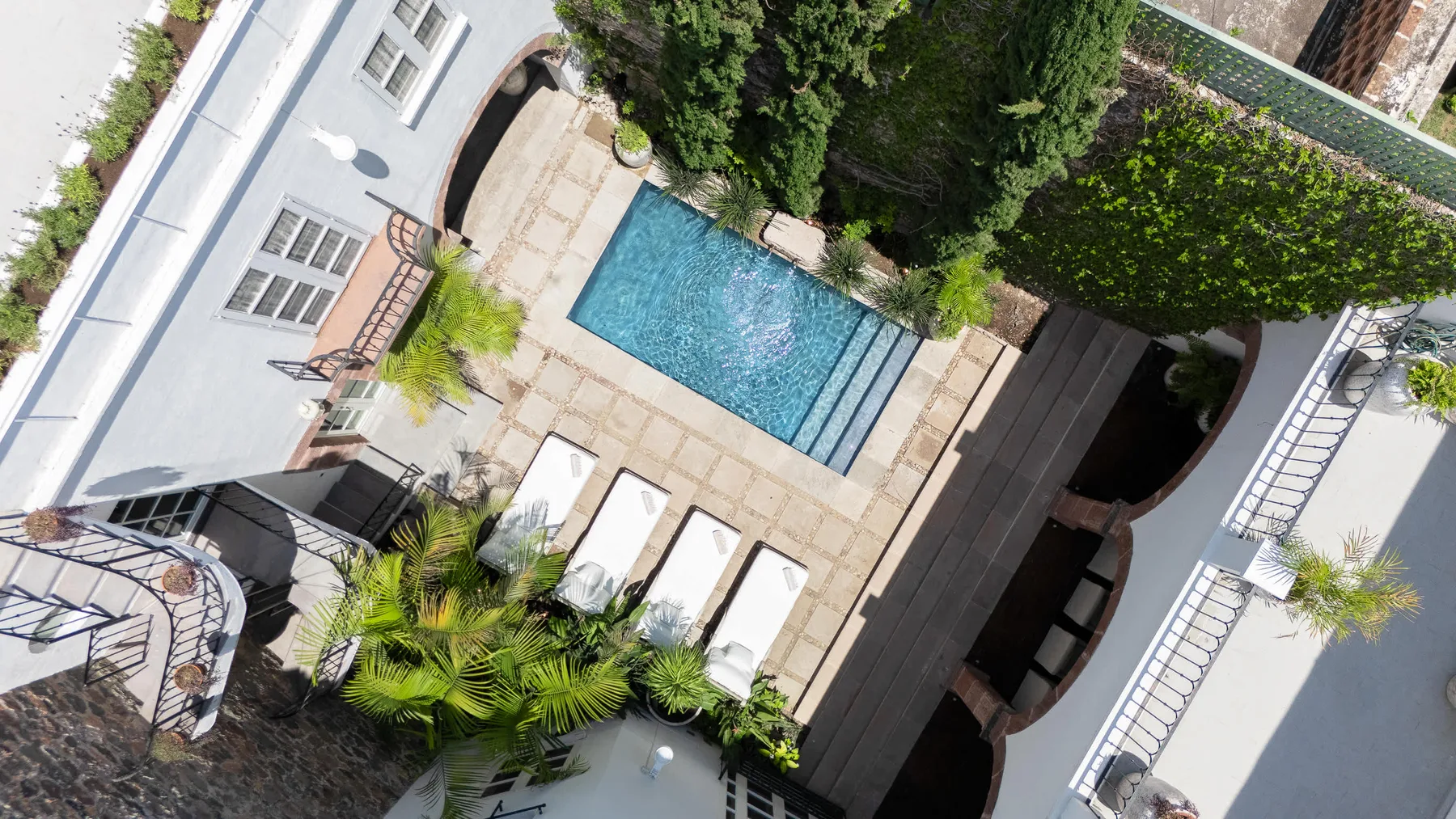 Vista aérea de una piscina en un patio, rodeada de zonas pavimentadas y vegetación.