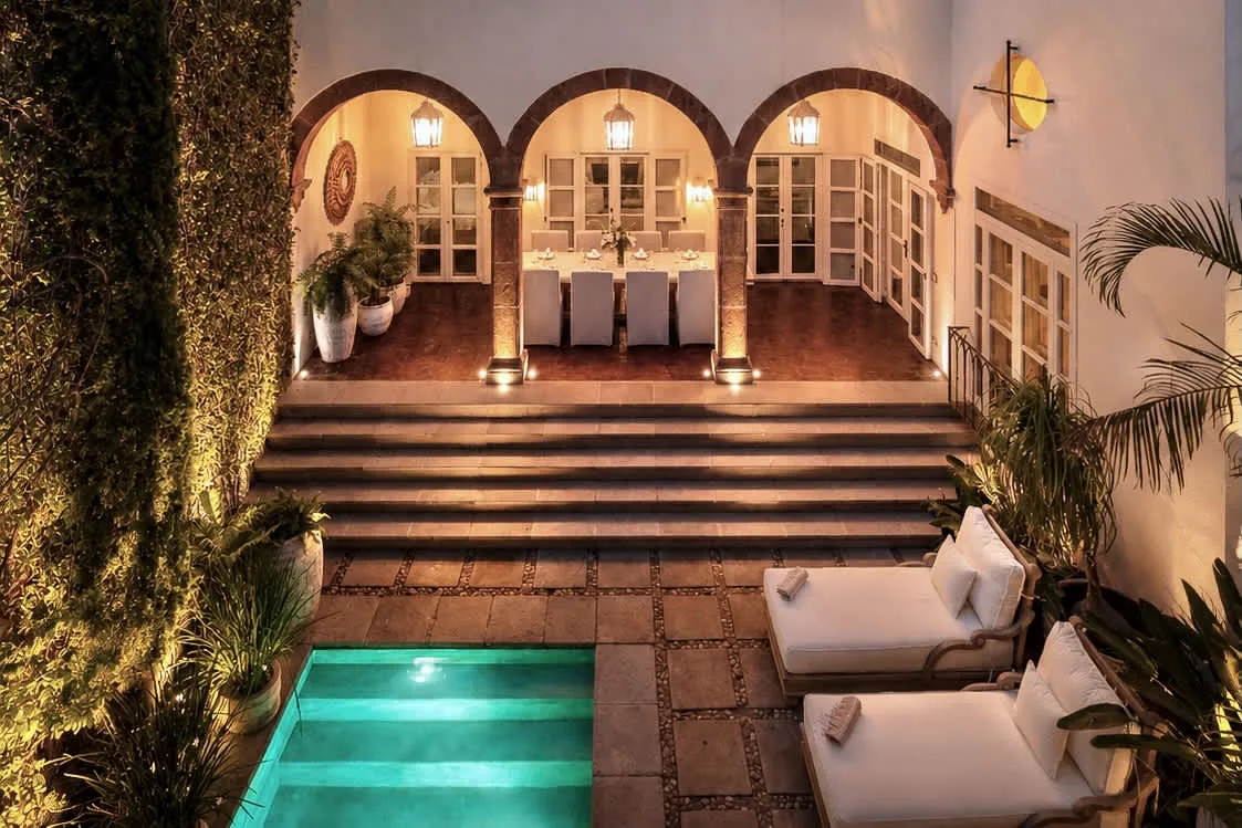 Una piscina y una zona de estar ocupan el patio, bajo un comedor con arcos.