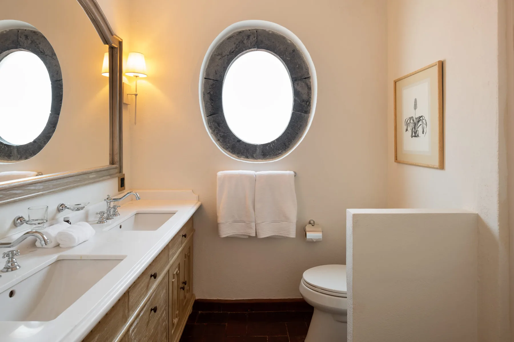 Un baño con lavabo, ventana ovalada e inodoro.