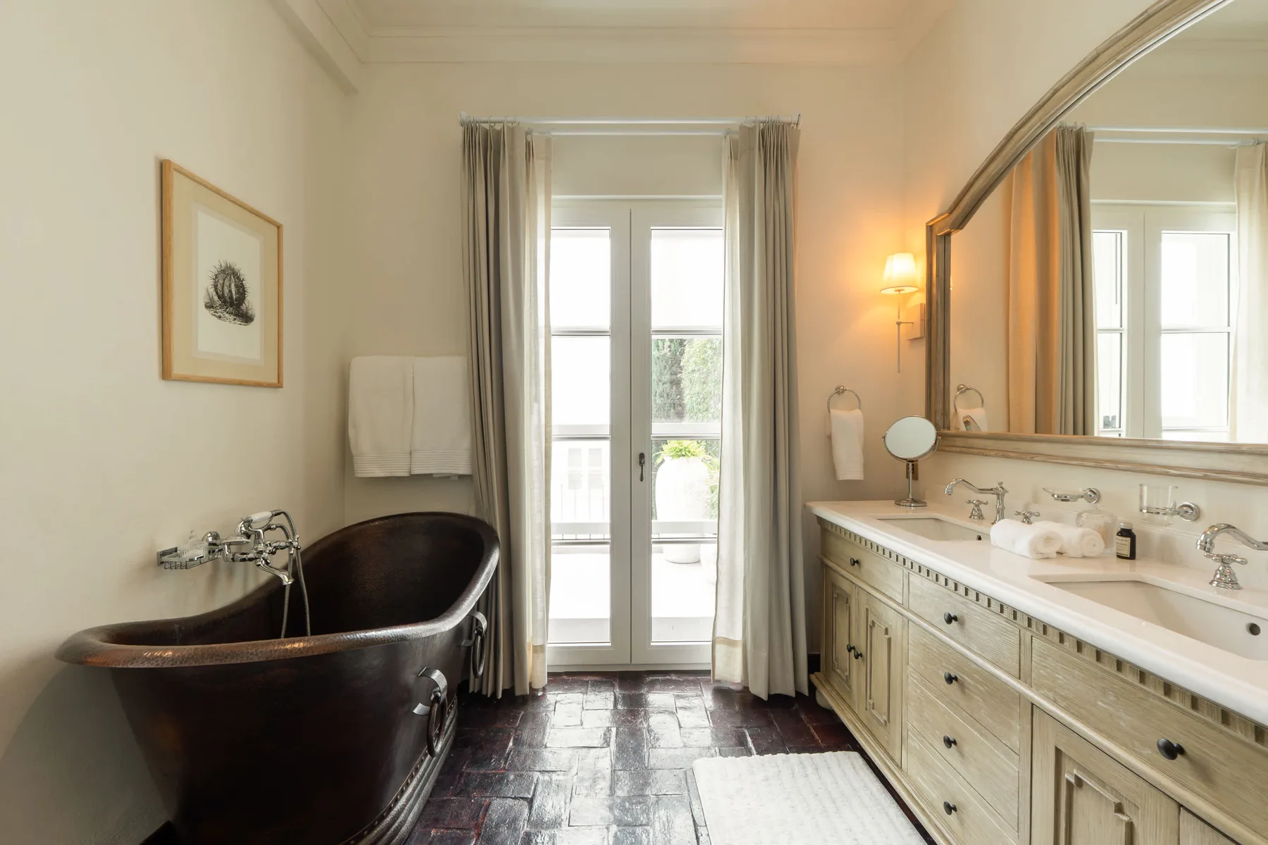 Un baño con una bañera exenta junto a un tocador largo y ventanas luminosas.