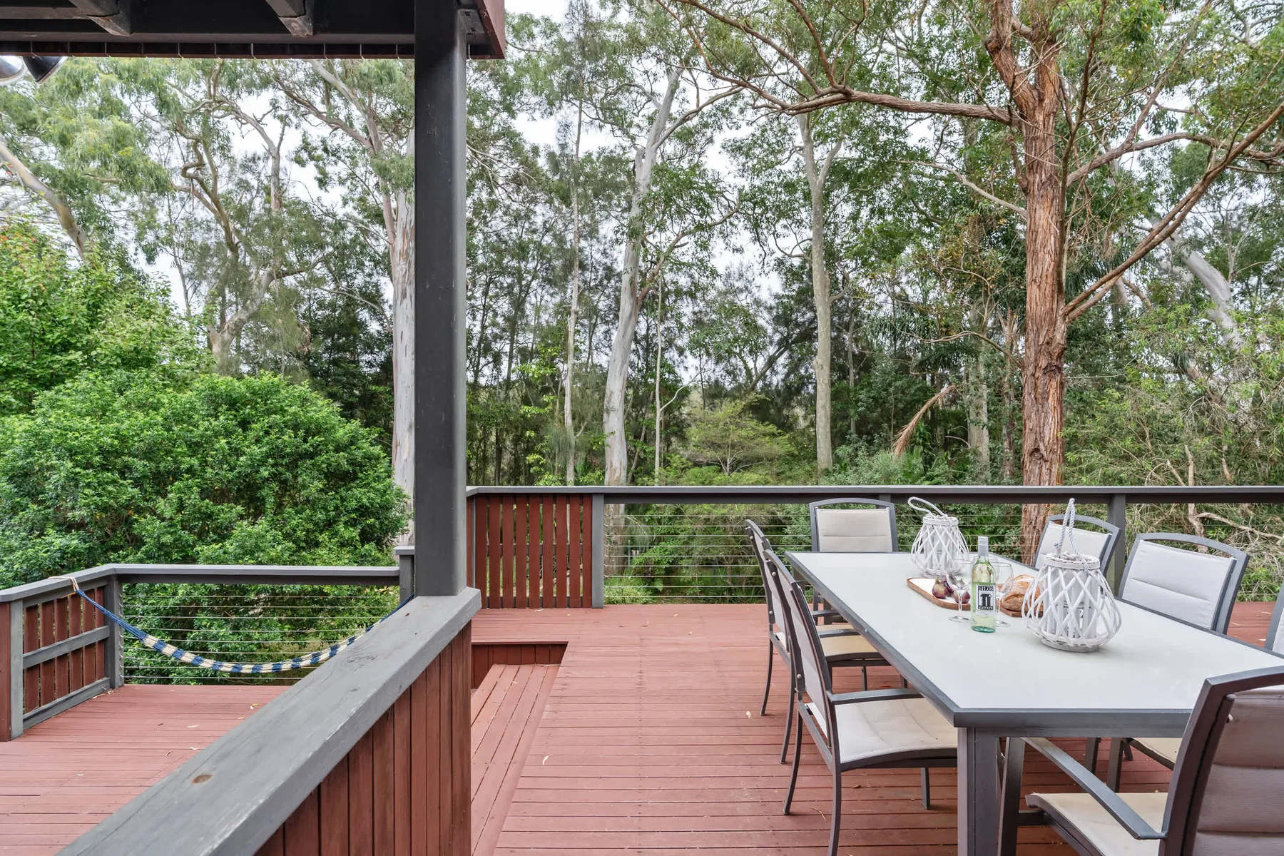 Una terraza exterior con una mesa de comedor da a una zona arbolada.