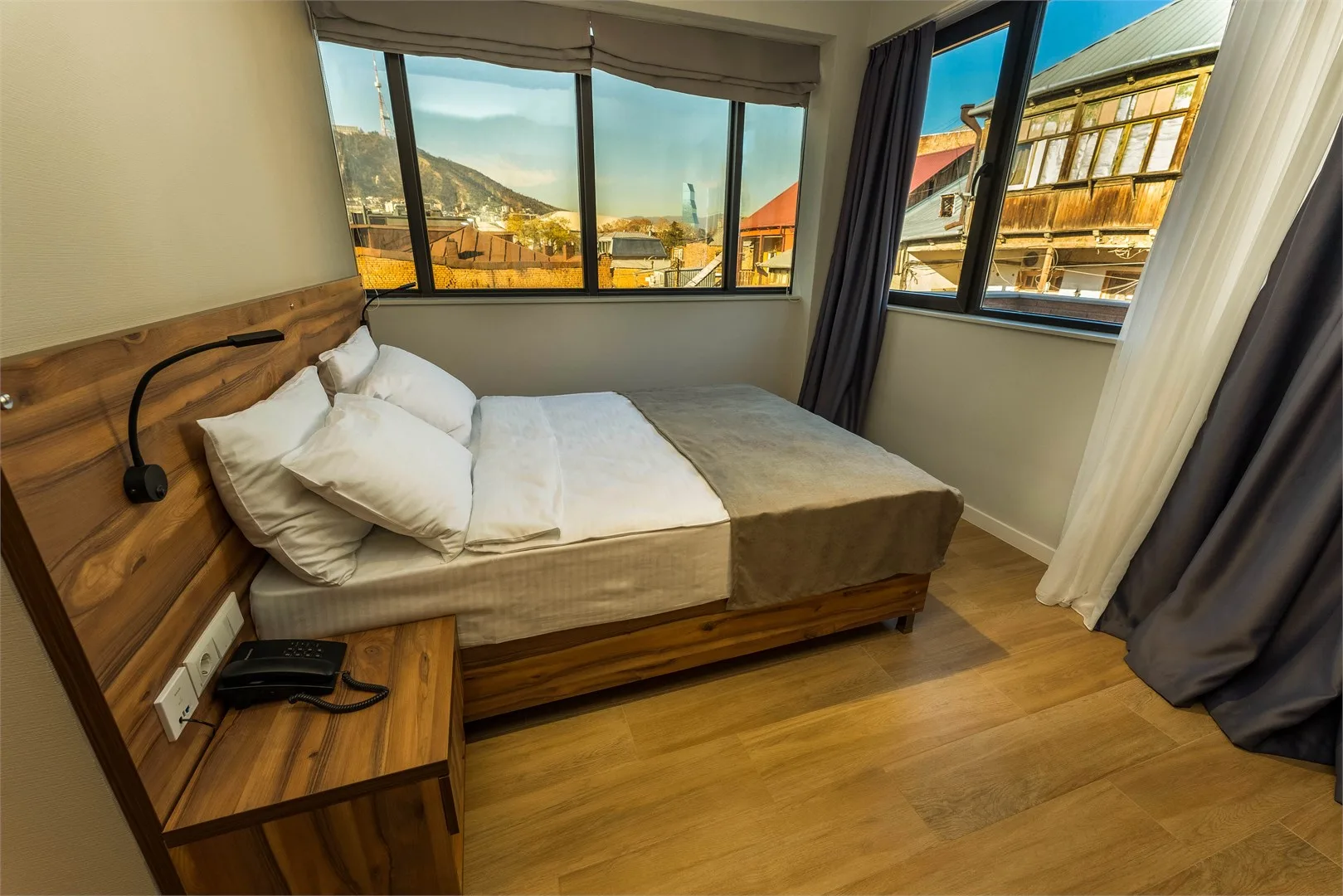 Representative hotel space: A bedroom with a wooden bed beside large windows overlooking nearby buildings.
