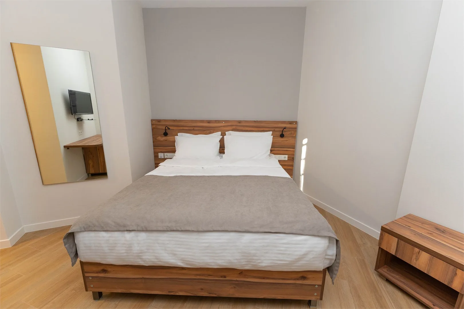 Representative hotel space: A bedroom with a wooden bed, white pillows, and a gray bedspread.