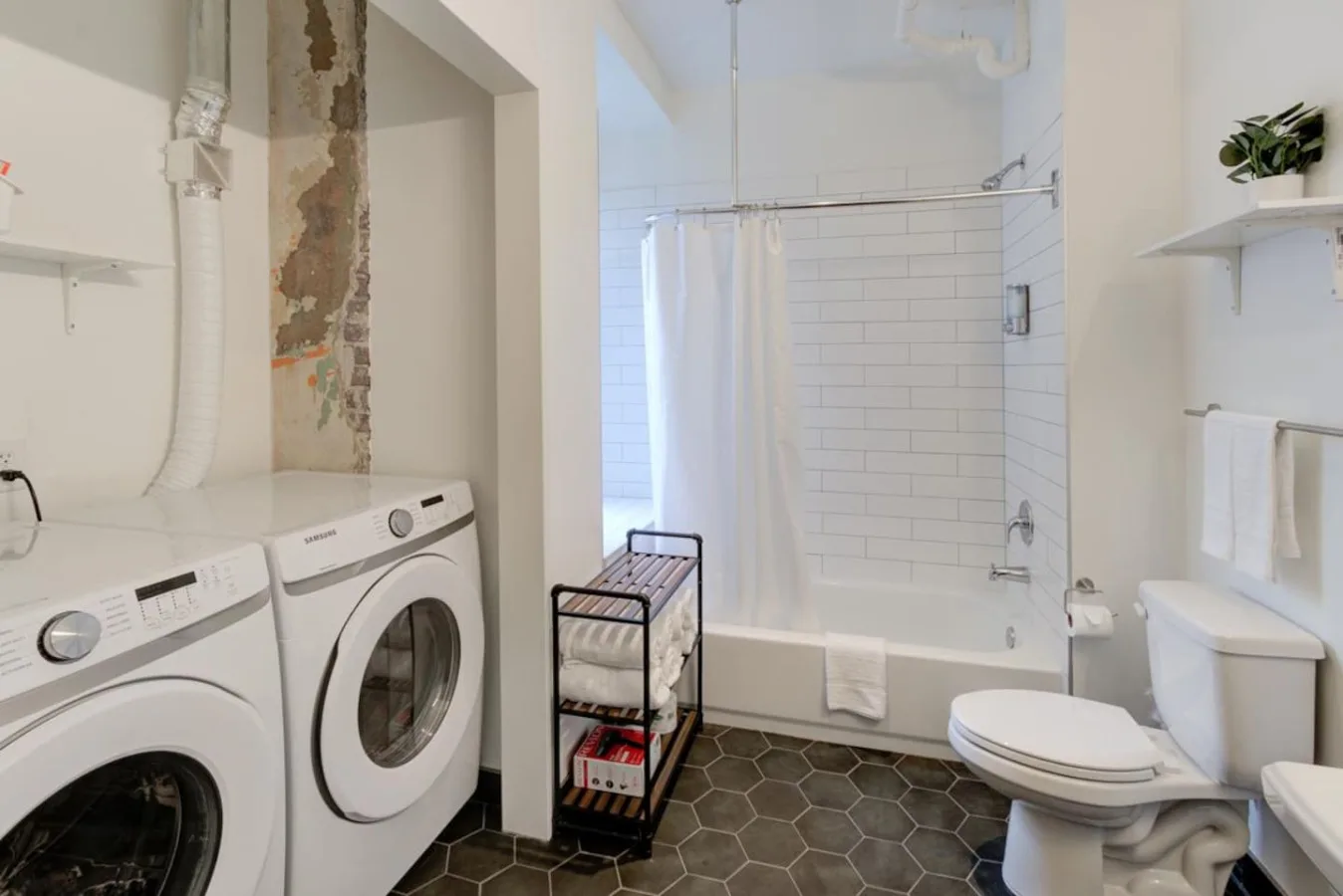 Un baño con bañera y ducha, inodoro y máquinas de lavandería.
