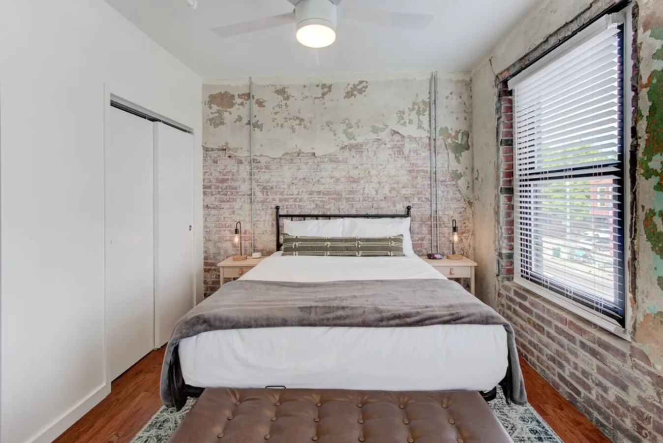 Un dormitorio con una cama, mesitas de noche y una ventana grande con persianas.