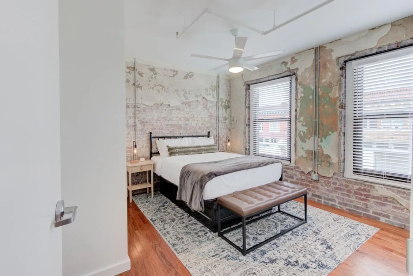 Un dormitorio con una cama, un banco y ventanas grandes con persianas.