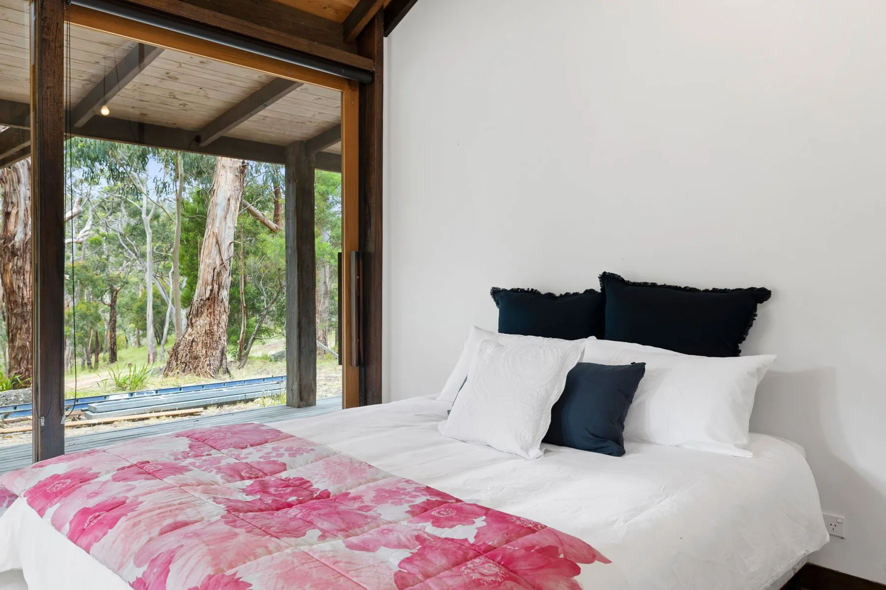 Bedroom with a bed beside large windows overlooking trees.