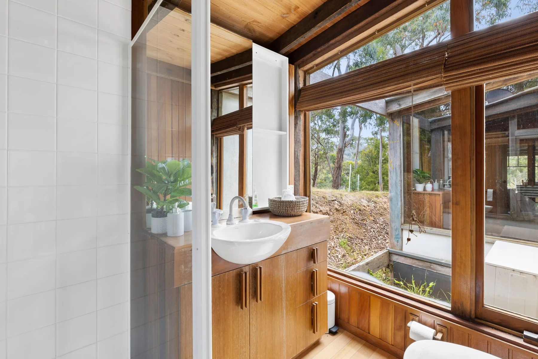 A bright bathroom with a sink beside large windows overlooking trees.