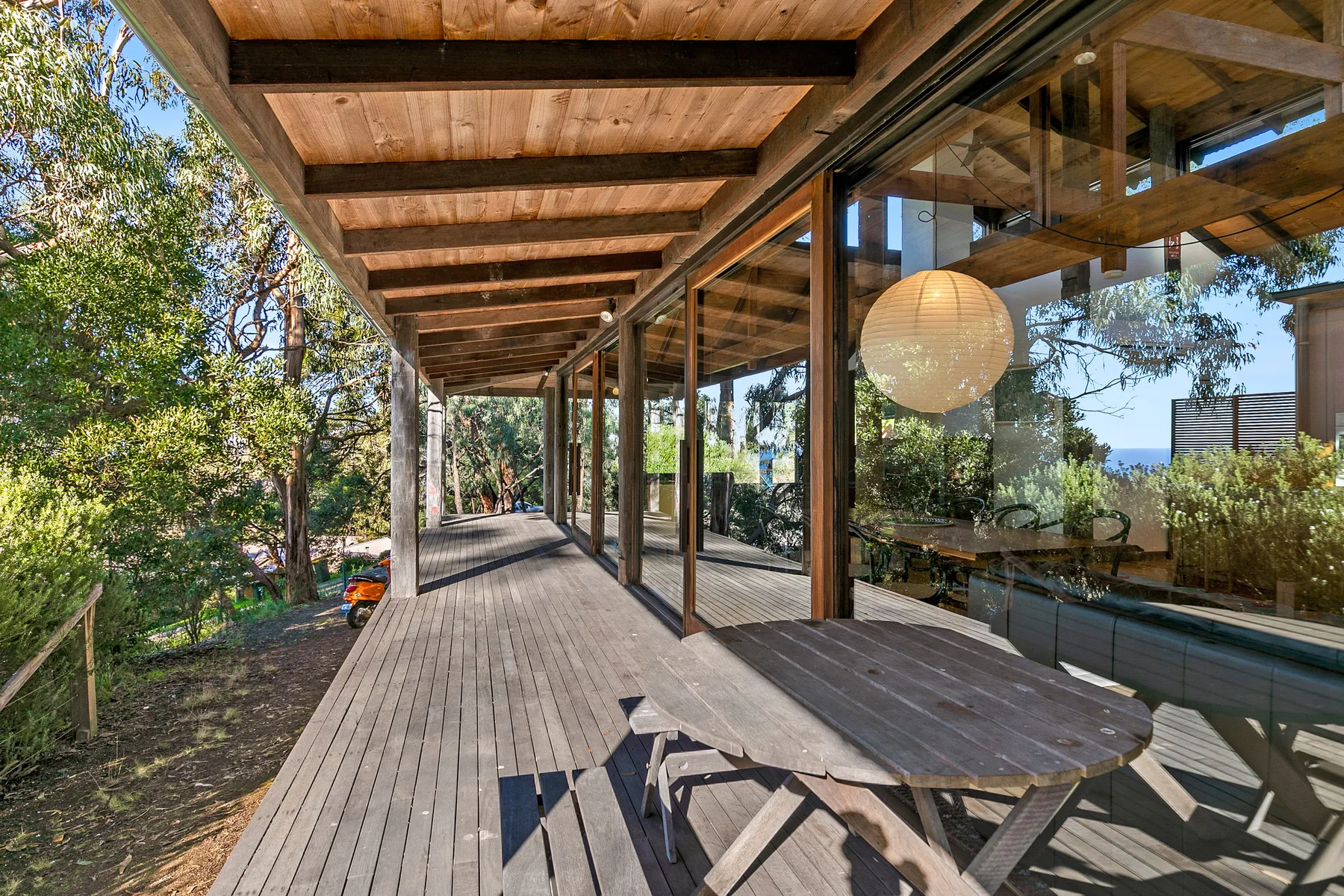 A covered wooden deck runs alongside a glass-walled room among trees.