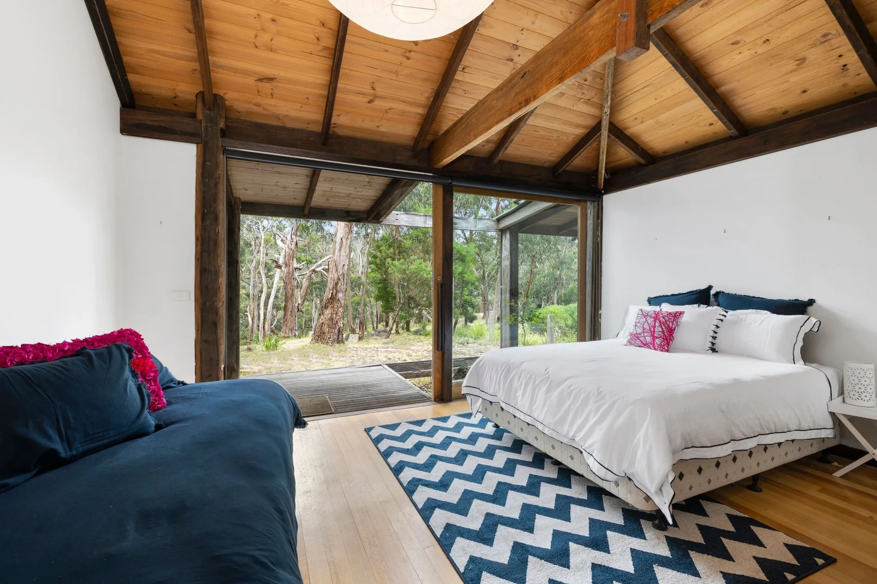 A bedroom with a bed, blue seating, and large windows overlooking trees.