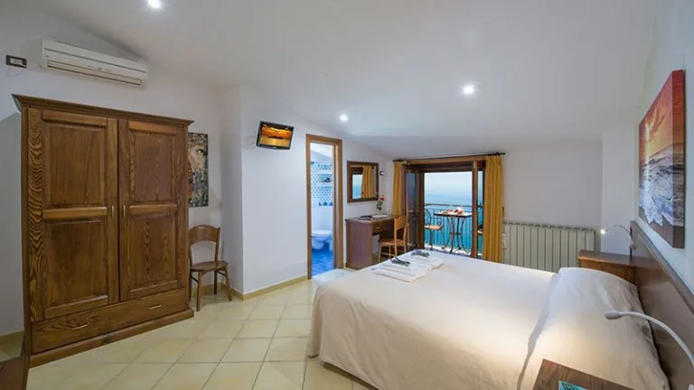 Espacio representativo del hotel: Un dormitorio con cama doble, armario de madera y vistas al mar.