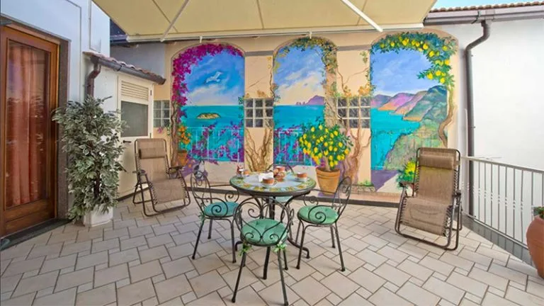Espacio representativo del hotel: Un patio exterior cubierto tiene murales marinos pintados y una mesa redonda con asientos.
