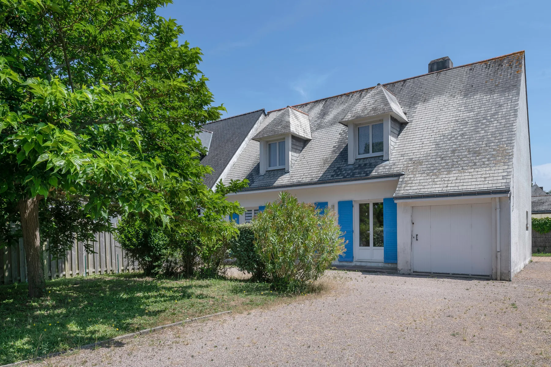 A white house with blue shutters and a gravel driveway.