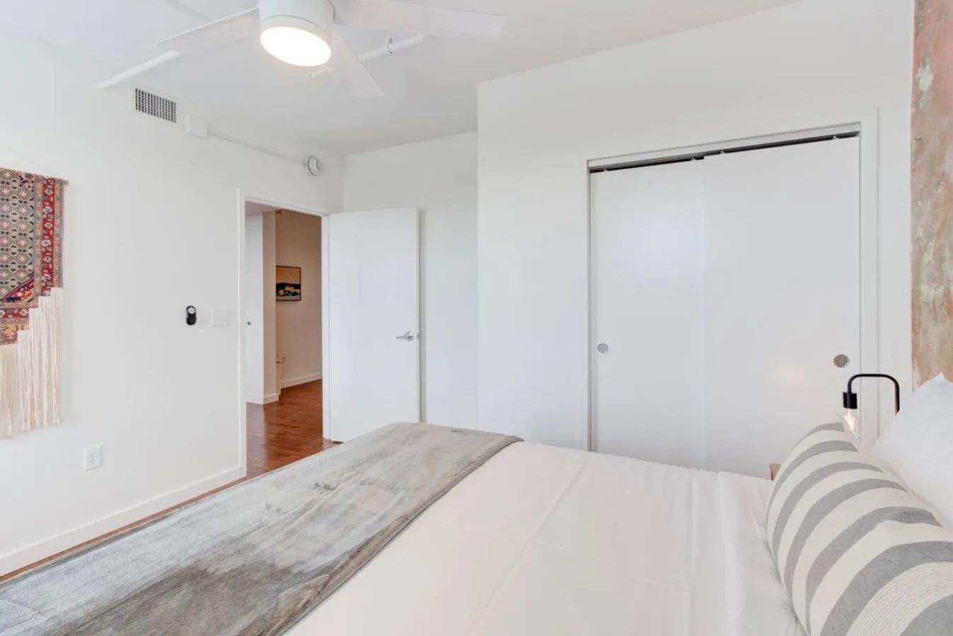 Un dormitorio luminoso con una cama, cojines a rayas y puertas correderas blancas.