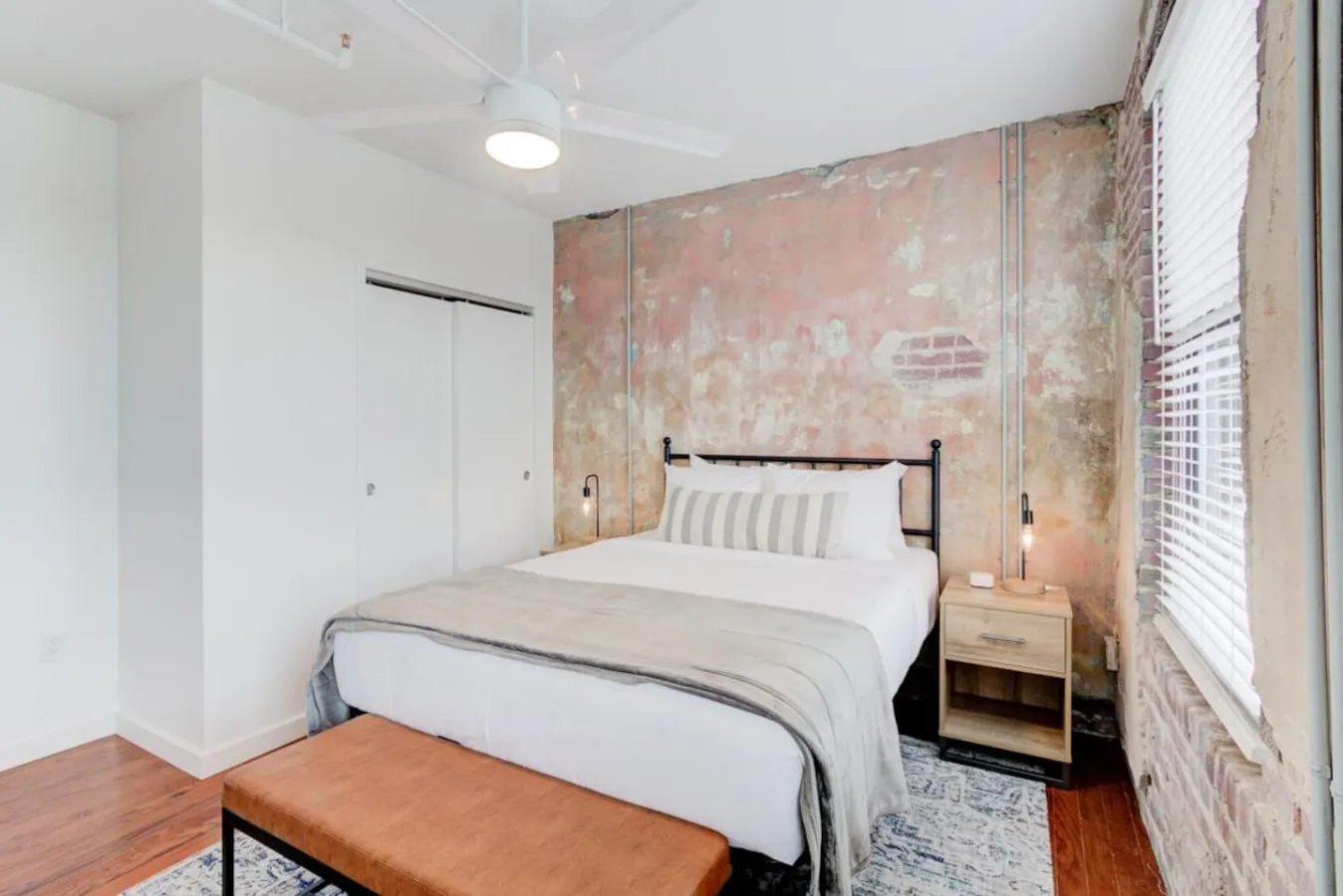 Un dormitorio con una cama tendida, una mesa de madera y una pared desgastada.