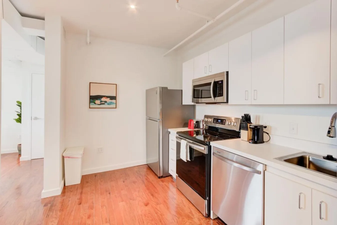 Una cocina luminosa con gabinetes blancos, electrodomésticos de acero inoxidable y piso de madera.