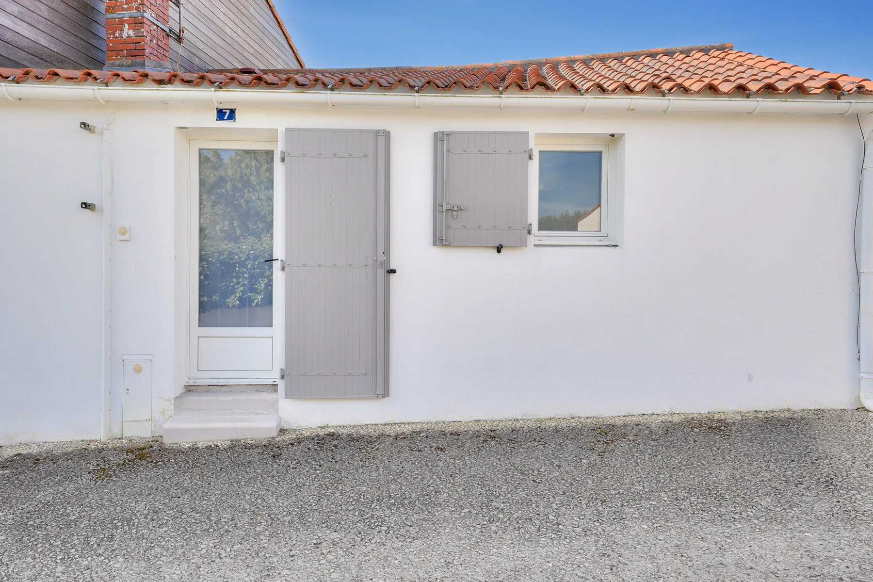 A white building facade with gray shutters and a tiled roof.