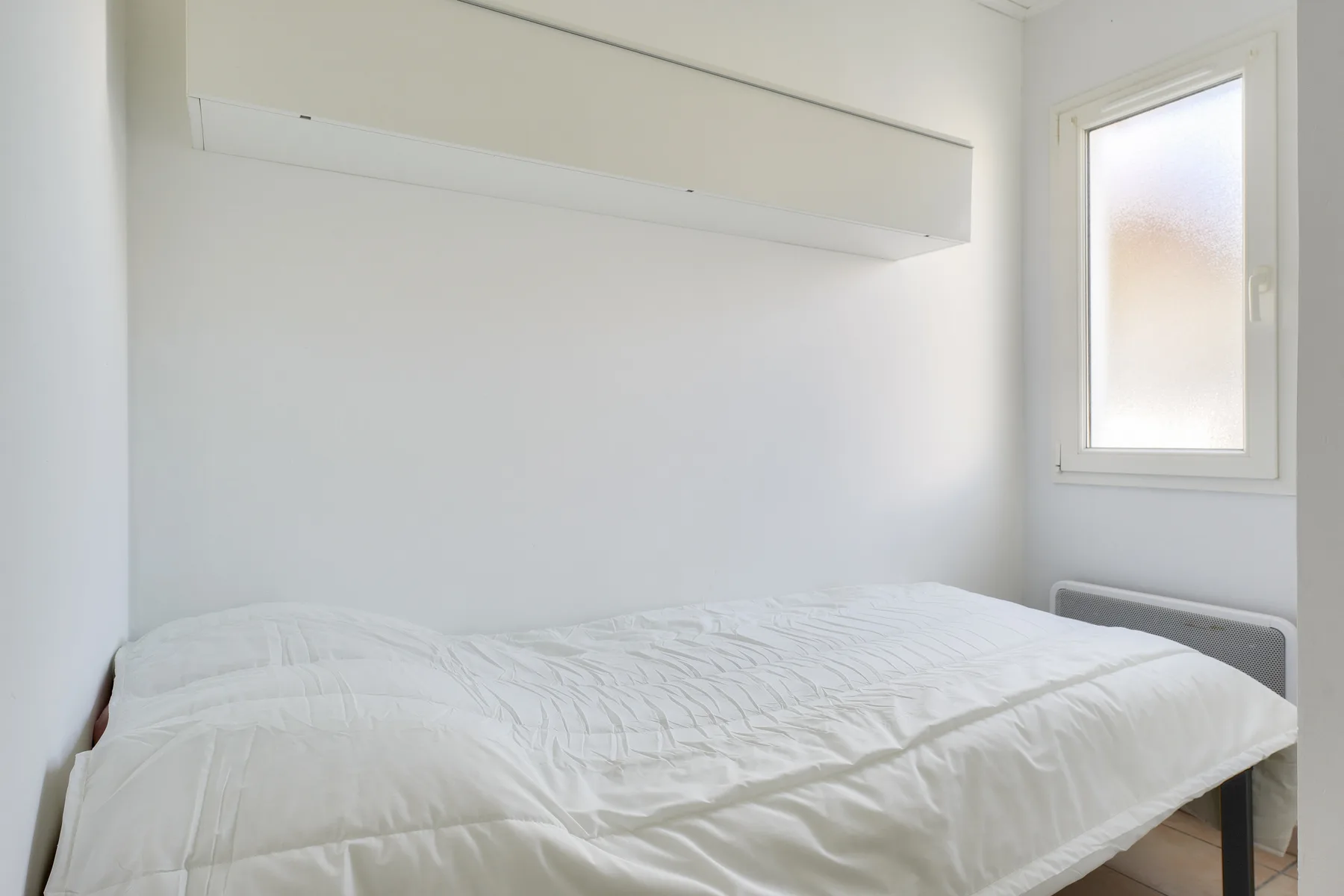 A bright bedroom with a bed beneath a wall-mounted shelf.