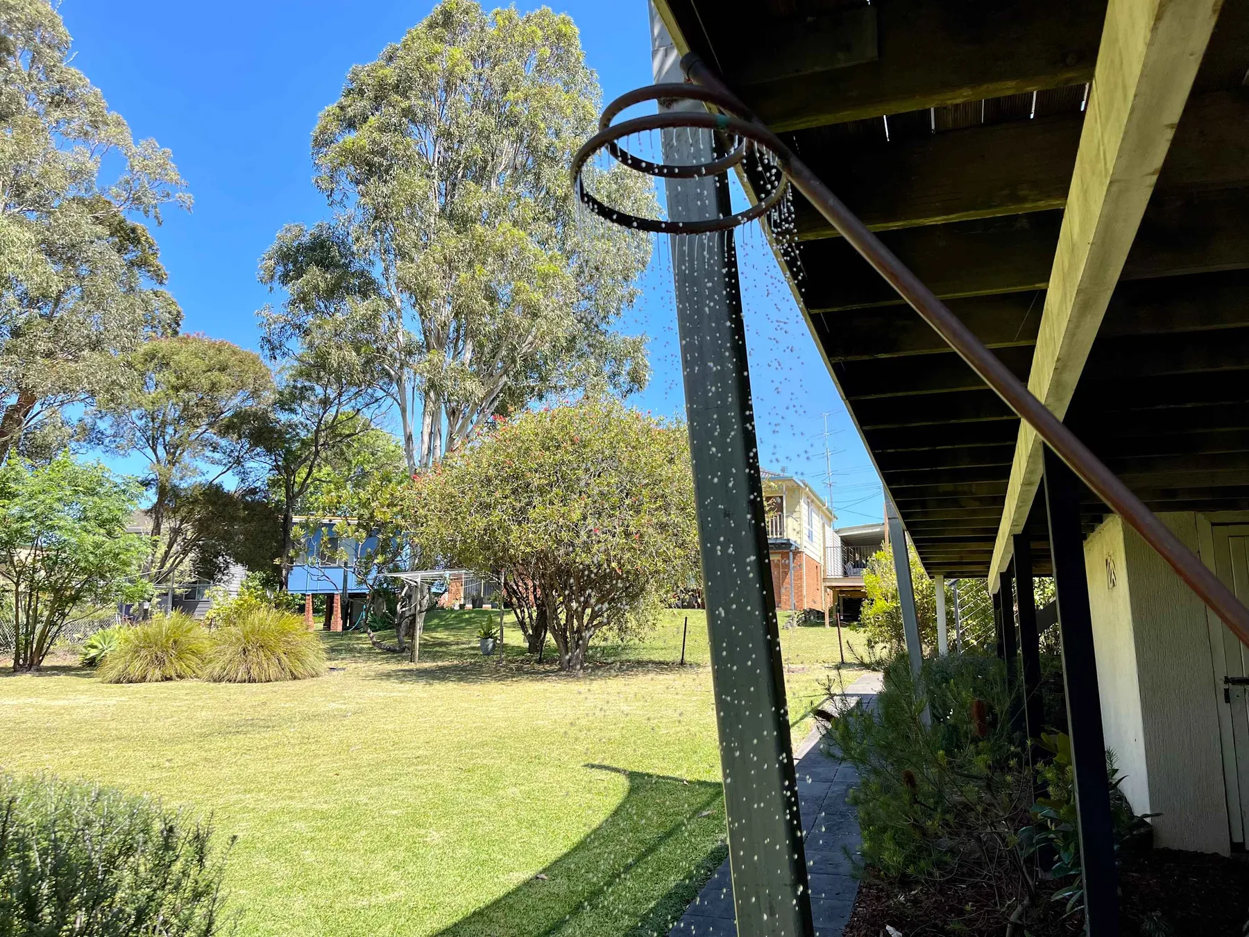 An outdoor shower stands beside a grassy yard with trees.