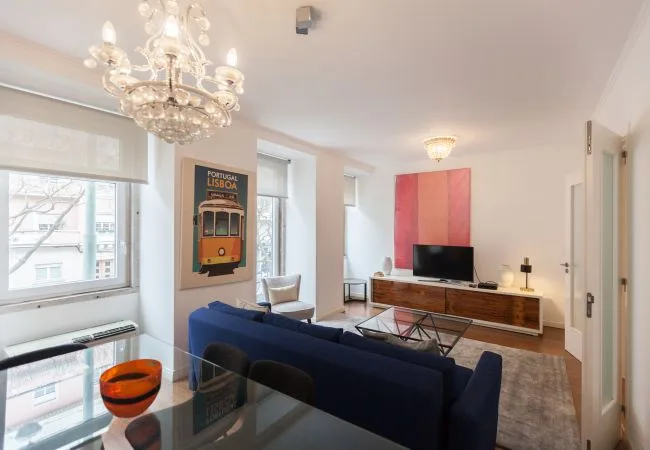 A living room with blue seating, a glass coffee table, and a television.