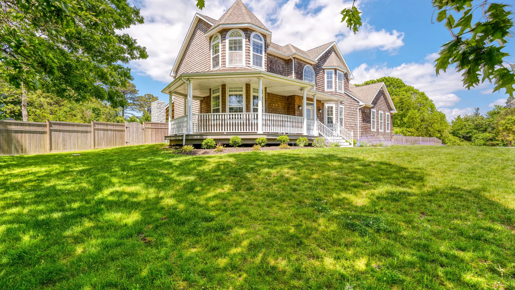 A large house with a wraparound porch sits behind a broad green lawn.