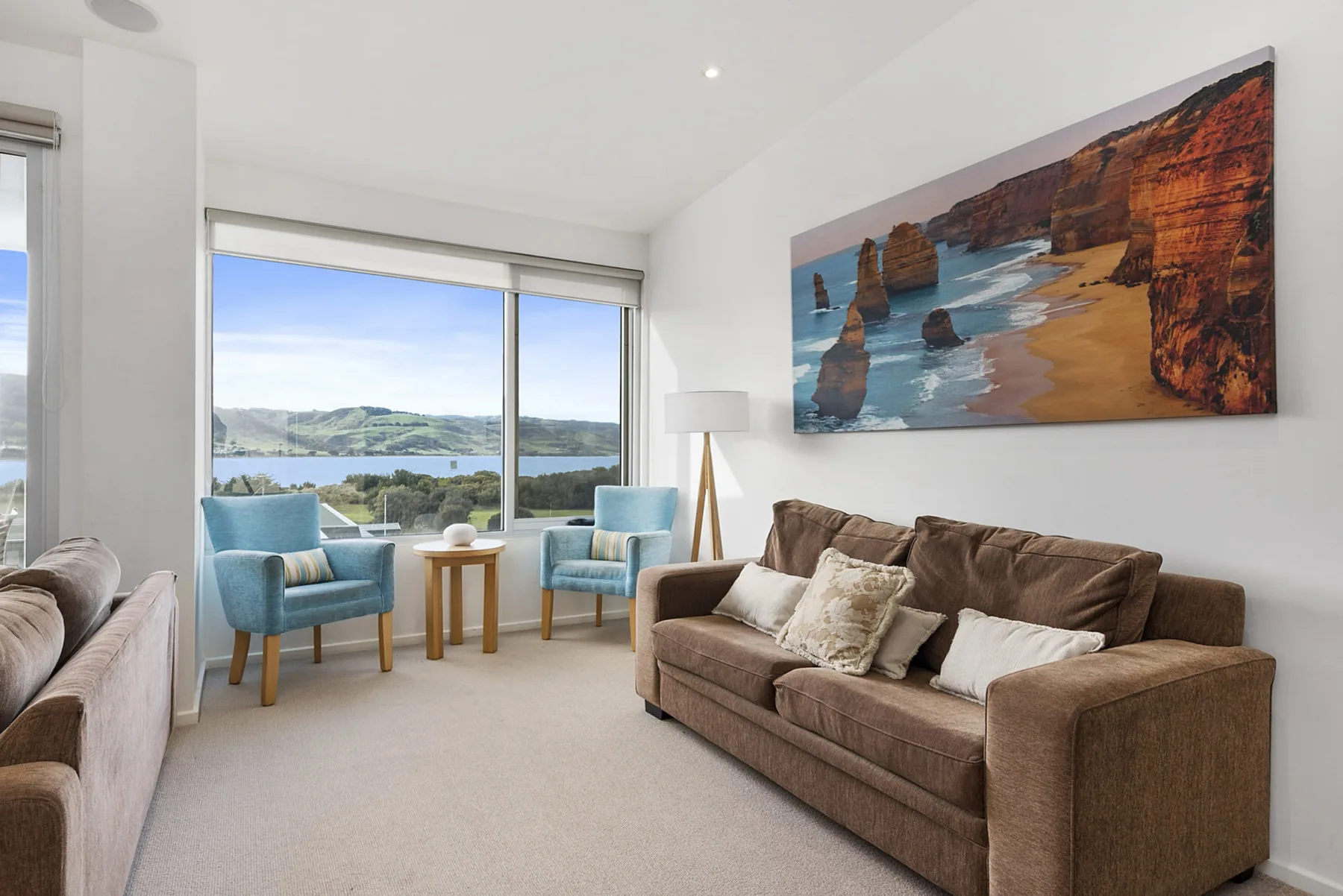 A bright living room with seating arranged beside large windows overlooking the water.