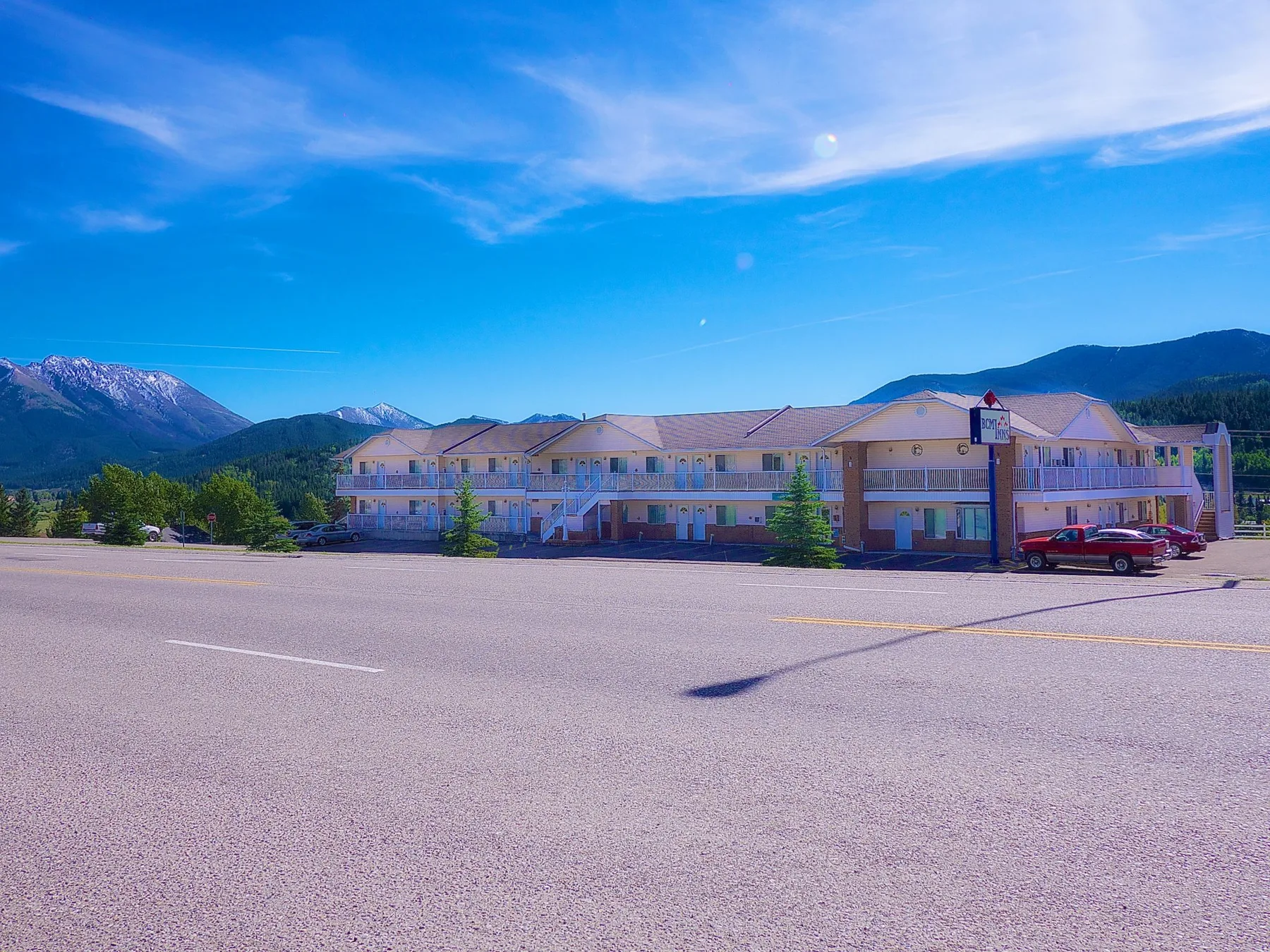 Representative hotel space: A hotel building stands beside a broad paved parking area, with mountains behind it.