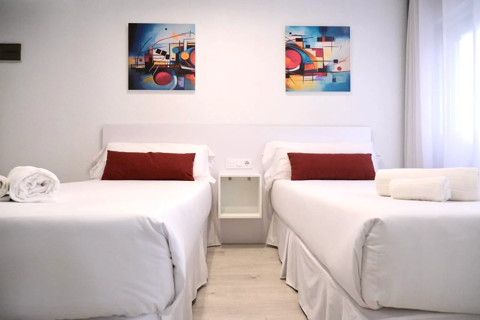 Espacio representativo del hotel: Un dormitorio luminoso con dos camas y cuadros coloridos en la pared.