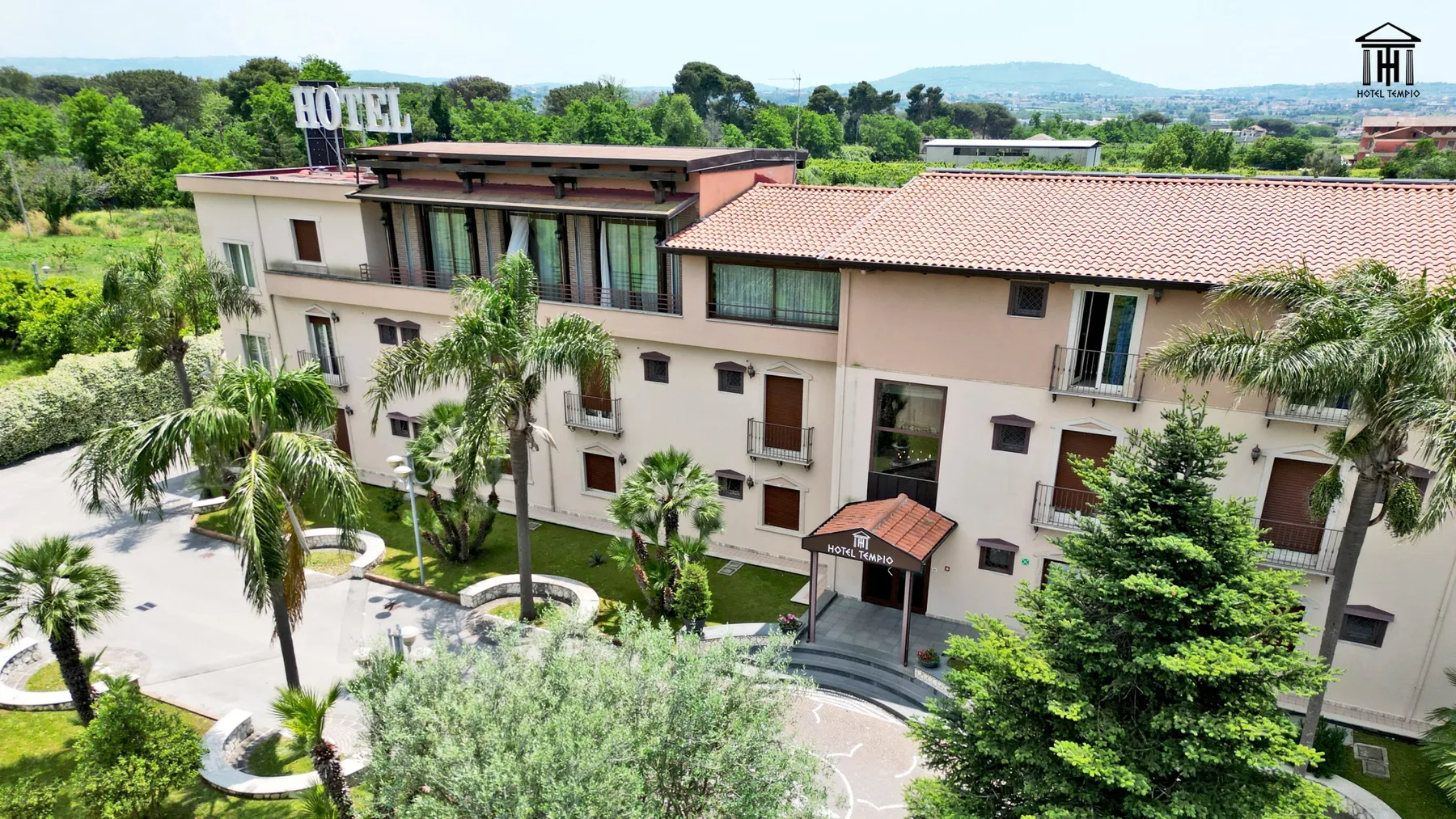 Representative hotel space: Hotel exterior surrounded by greenery, with a paved courtyard in front.