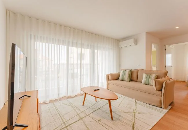 Una sala de estar luminosa con sofá, mesa de centro y cortinas translúcidas.