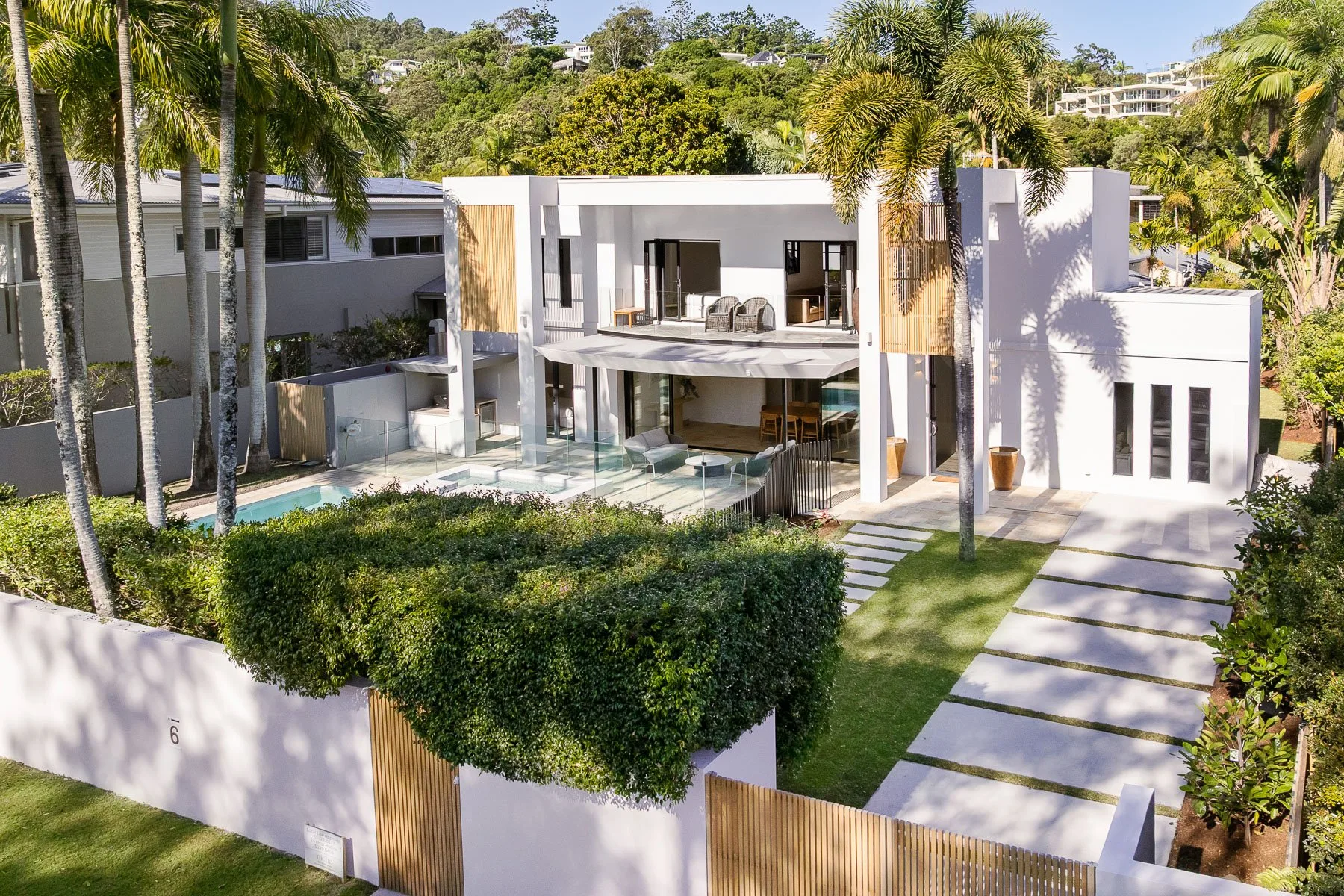 Modern house exterior with a swimming pool, landscaped garden, and palm trees.