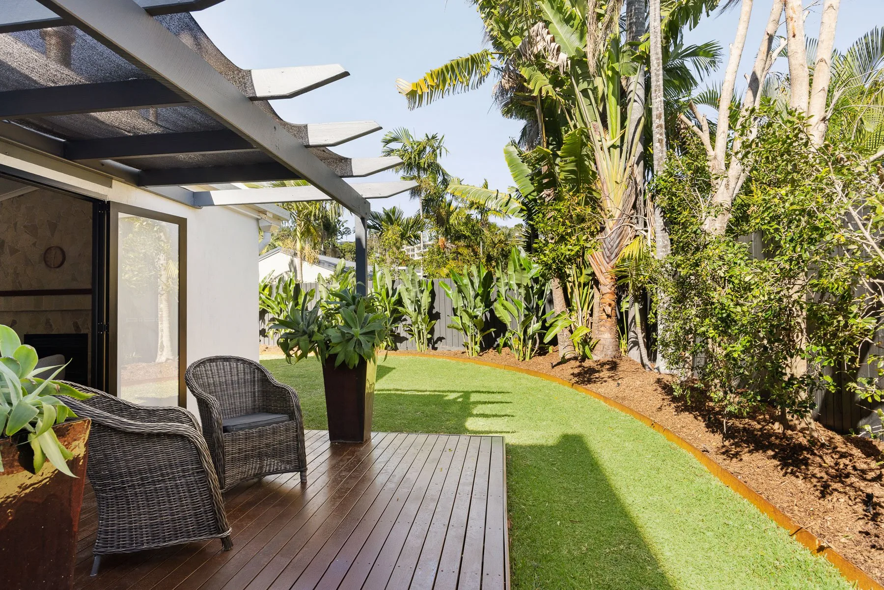 A covered patio with outdoor seating overlooks a green lawn and tropical plants.