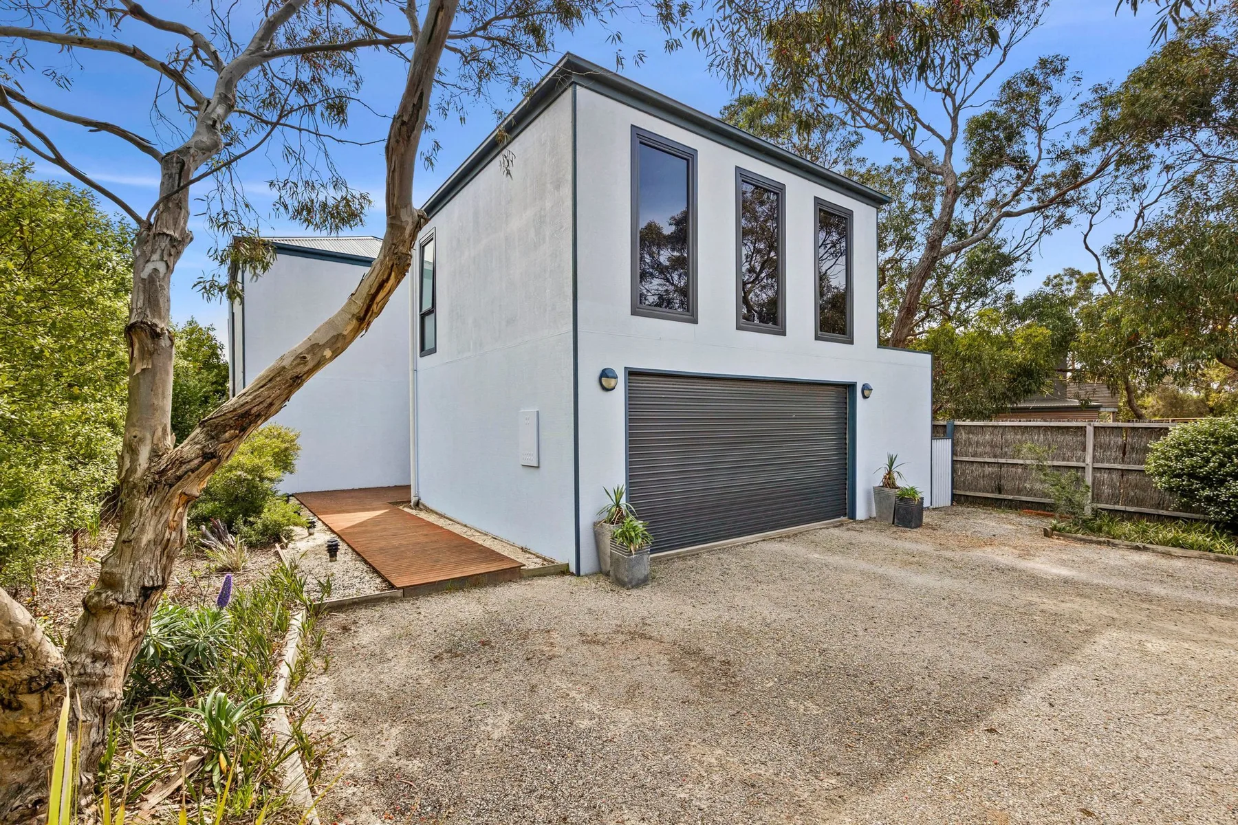 A modern white building with a dark garage door stands among trees.