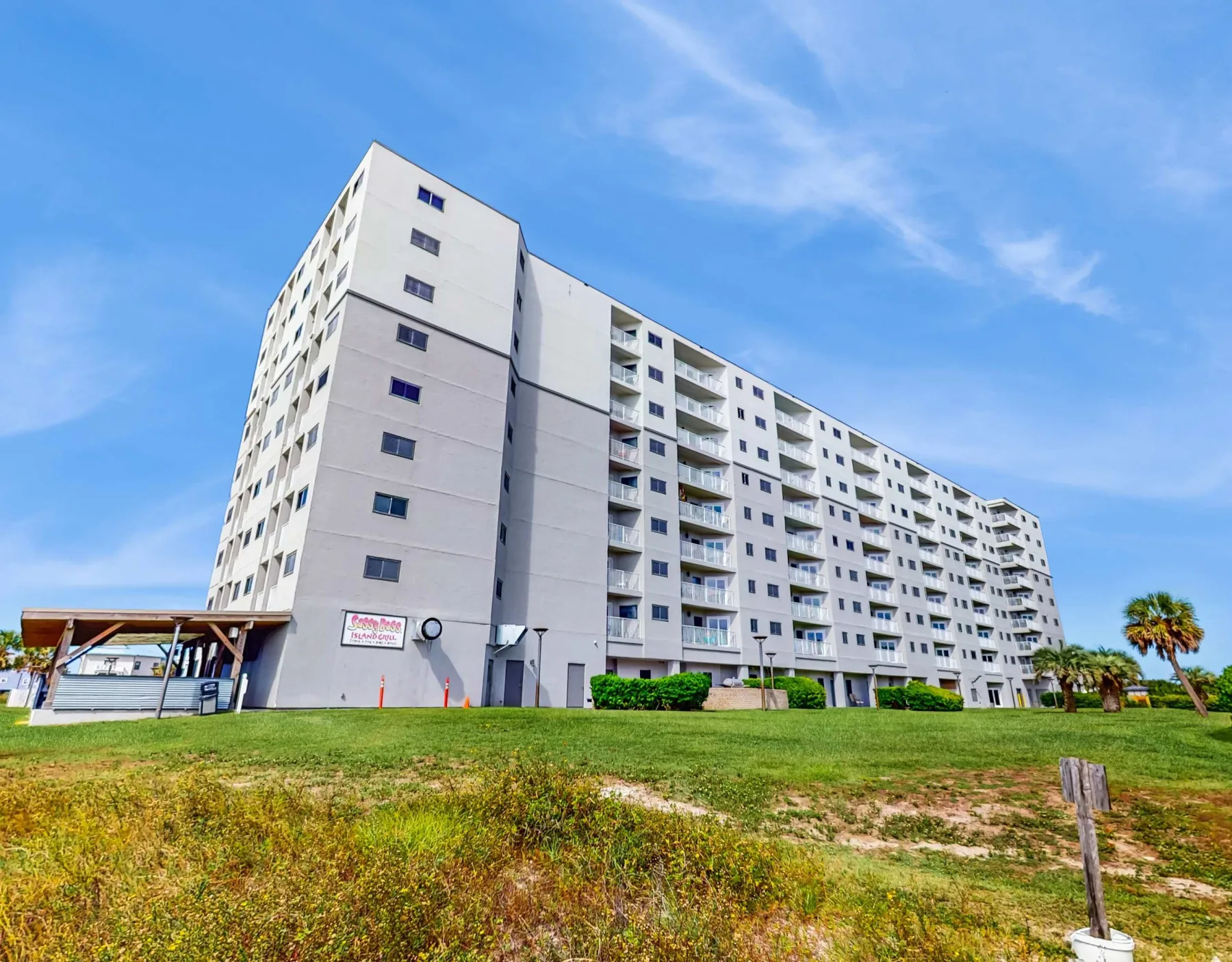 Zona común: Un gran edificio de apartamentos se alza junto a un césped bajo un cielo azul.