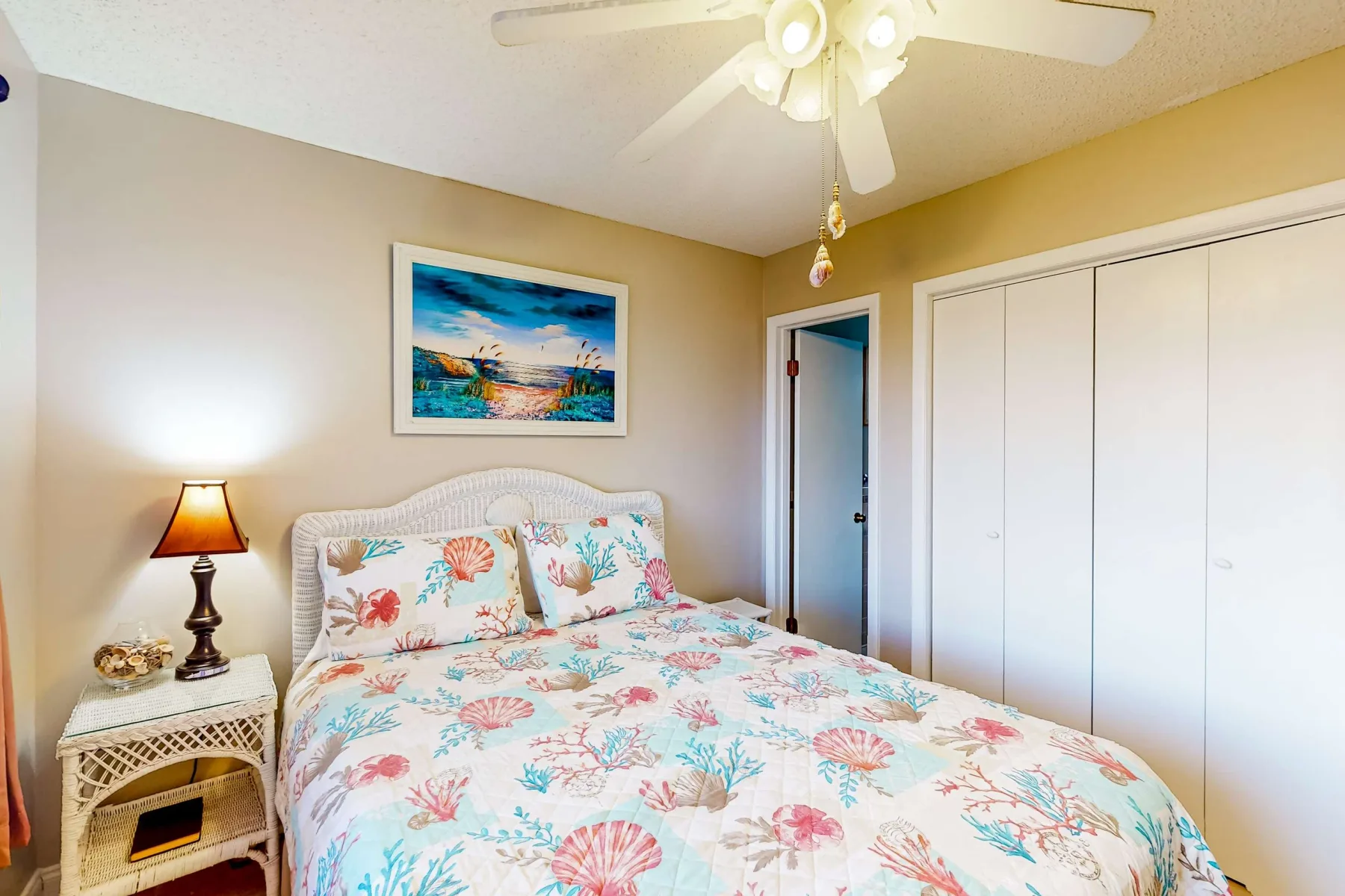 Un dormitorio con una cama cubierta con ropa de cama floral colorida y una mesita de noche.