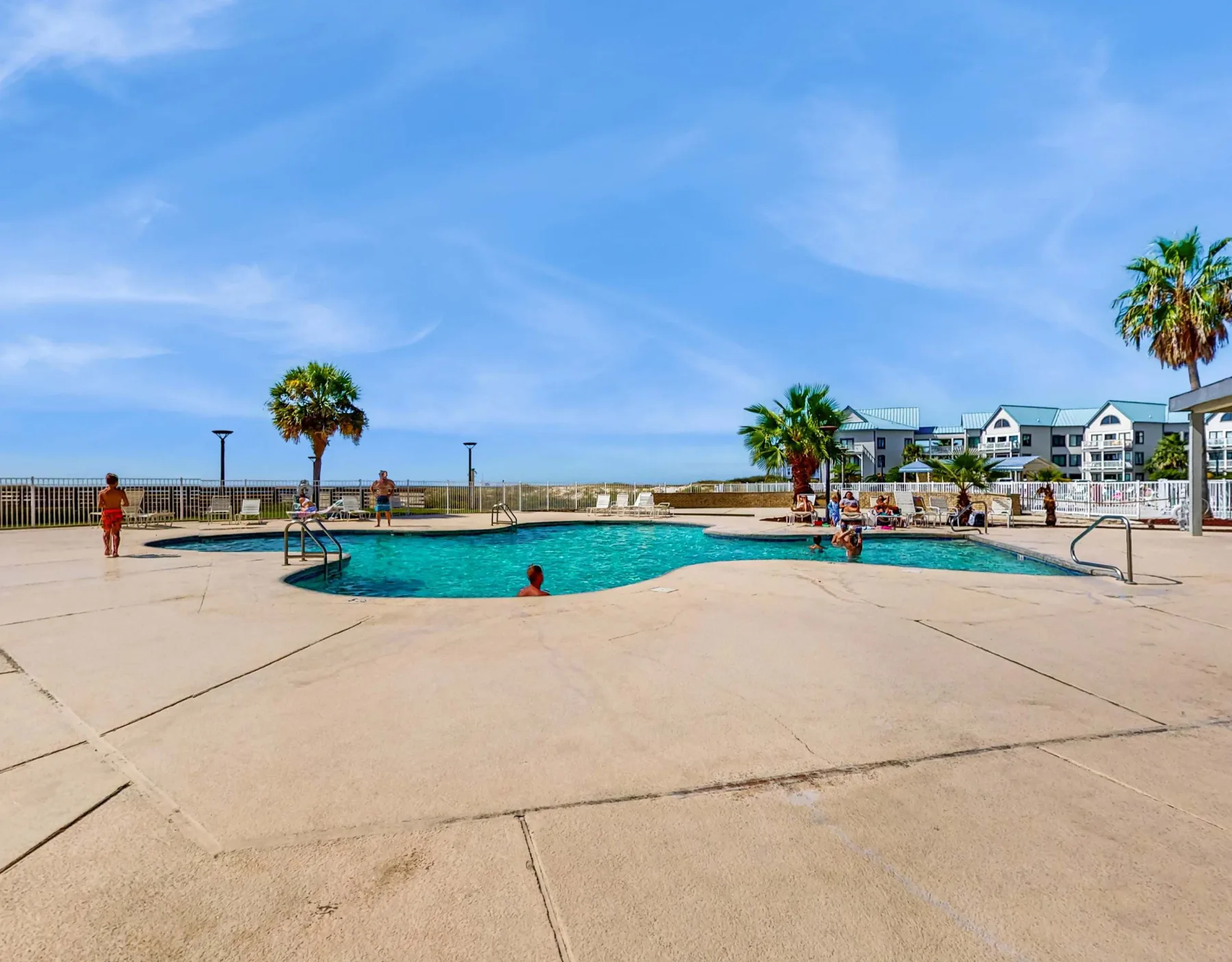 Zona común: Una piscina al aire libre con personas en el agua y palmeras cerca.