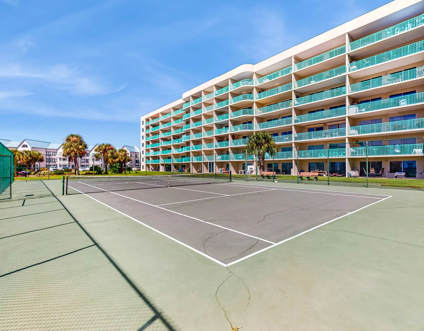 Zona común: Pista de tenis al aire libre junto a un edificio de varias plantas con balcones.