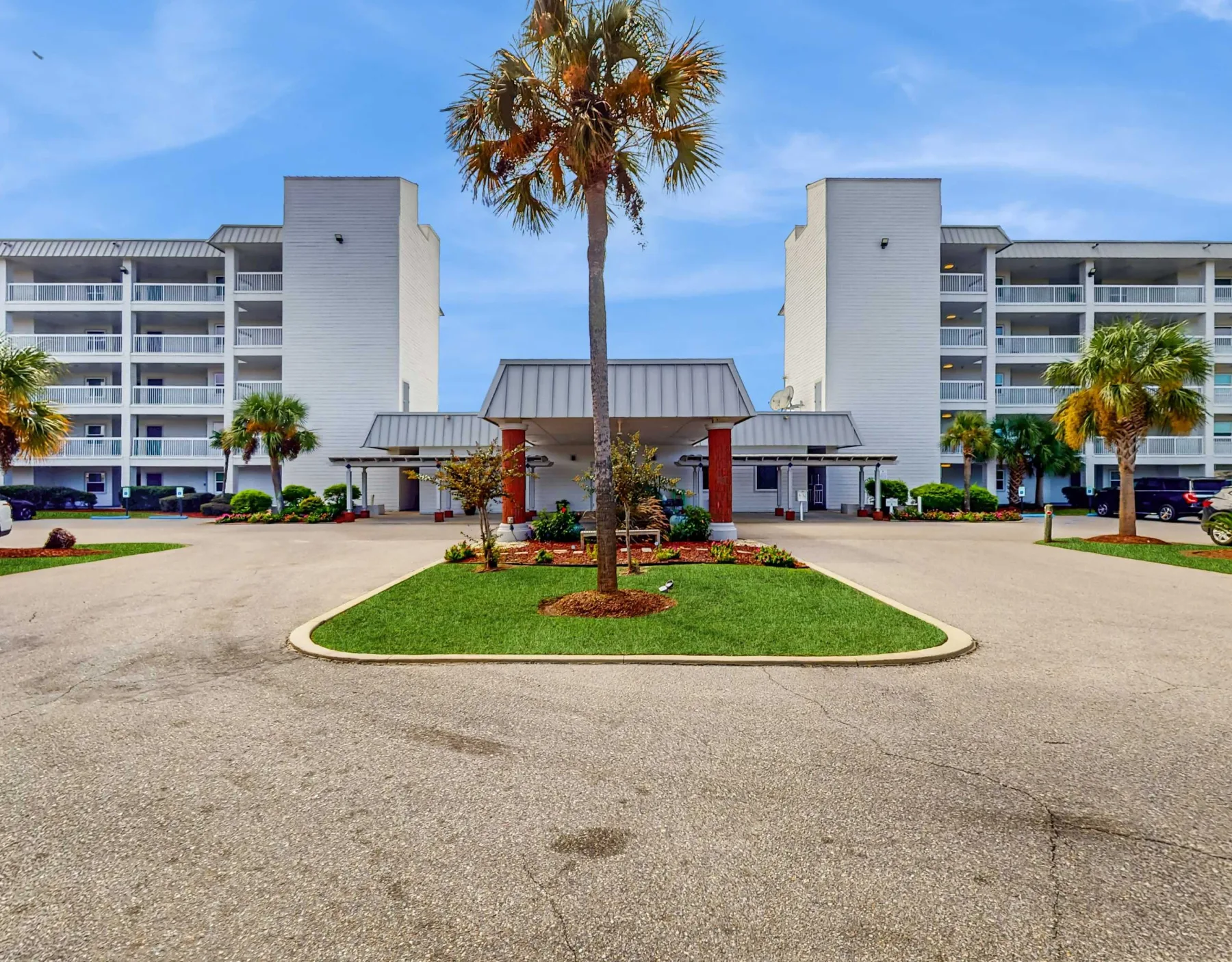 Zona común: Entrada de un edificio de varios pisos con una palmera en la rotonda.