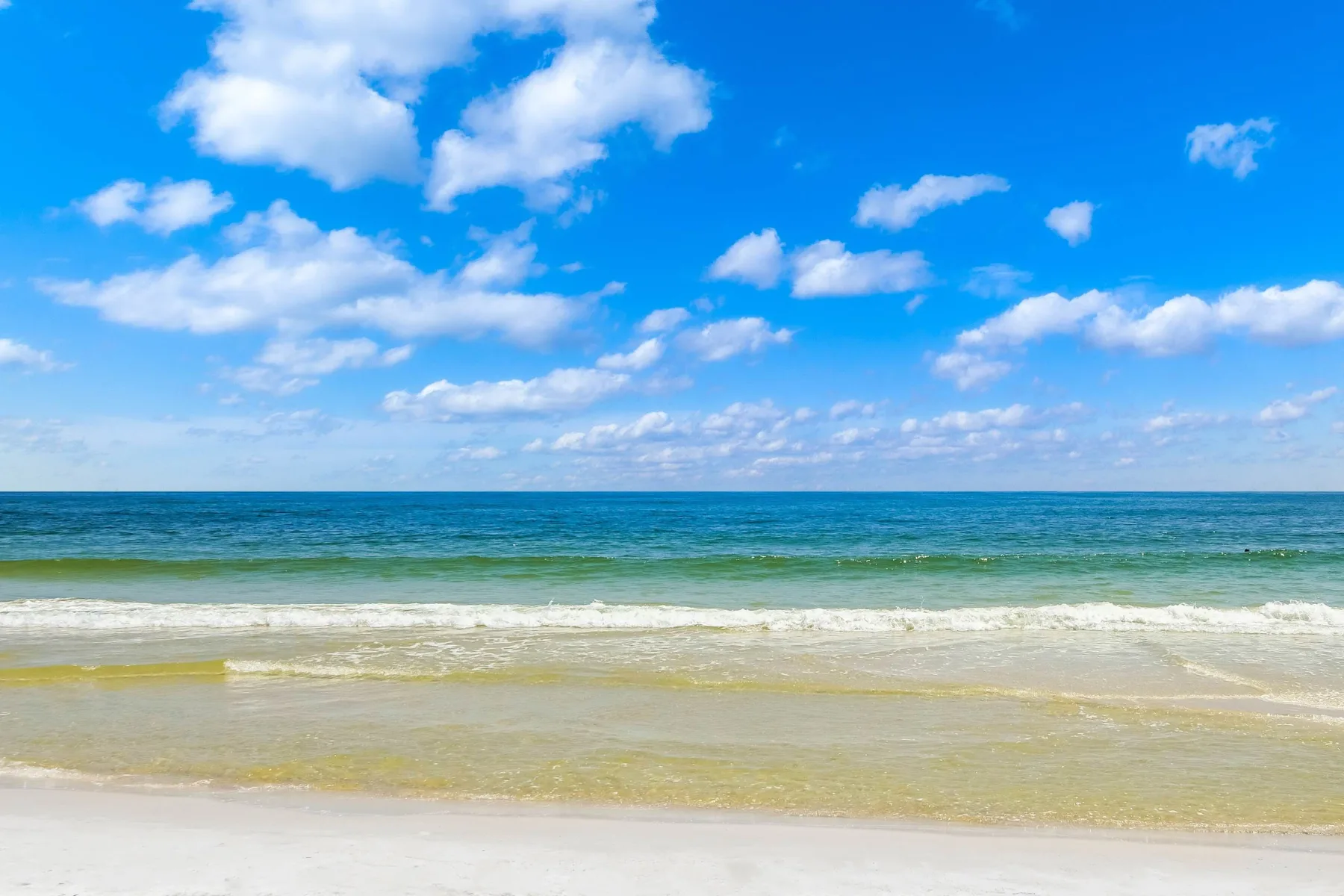 Zona común: Una playa de arena se encuentra con olas tranquilas bajo un cielo parcialmente nublado.