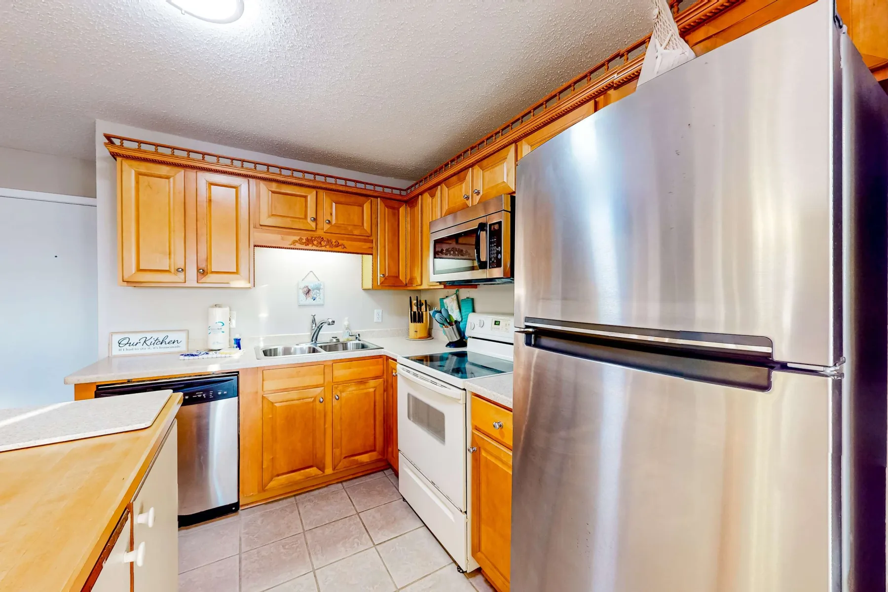 Una cocina con gabinetes de madera, un refrigerador de acero inoxidable y piso de baldosas.