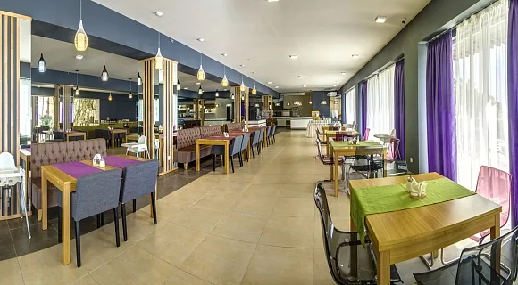 Espacio representativo del hotel: Un comedor con mesas y sillas junto a grandes ventanales con cortinas.