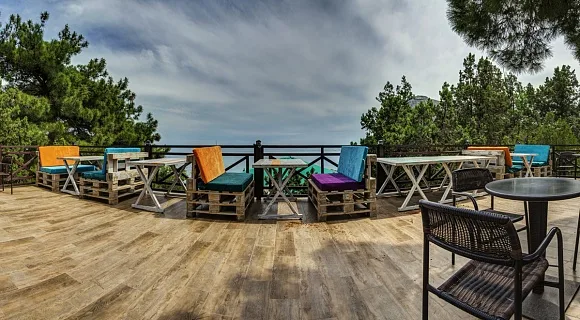 Espacio representativo del hotel: Una terraza exterior de madera tiene asientos coloridos y mesas, con árboles al fondo.