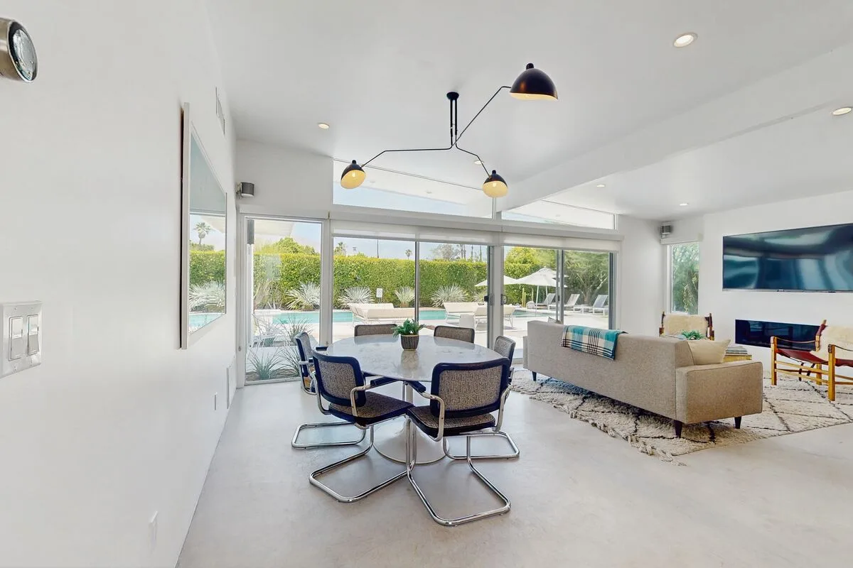 A bright living room with seating around a dining table and large windows.
