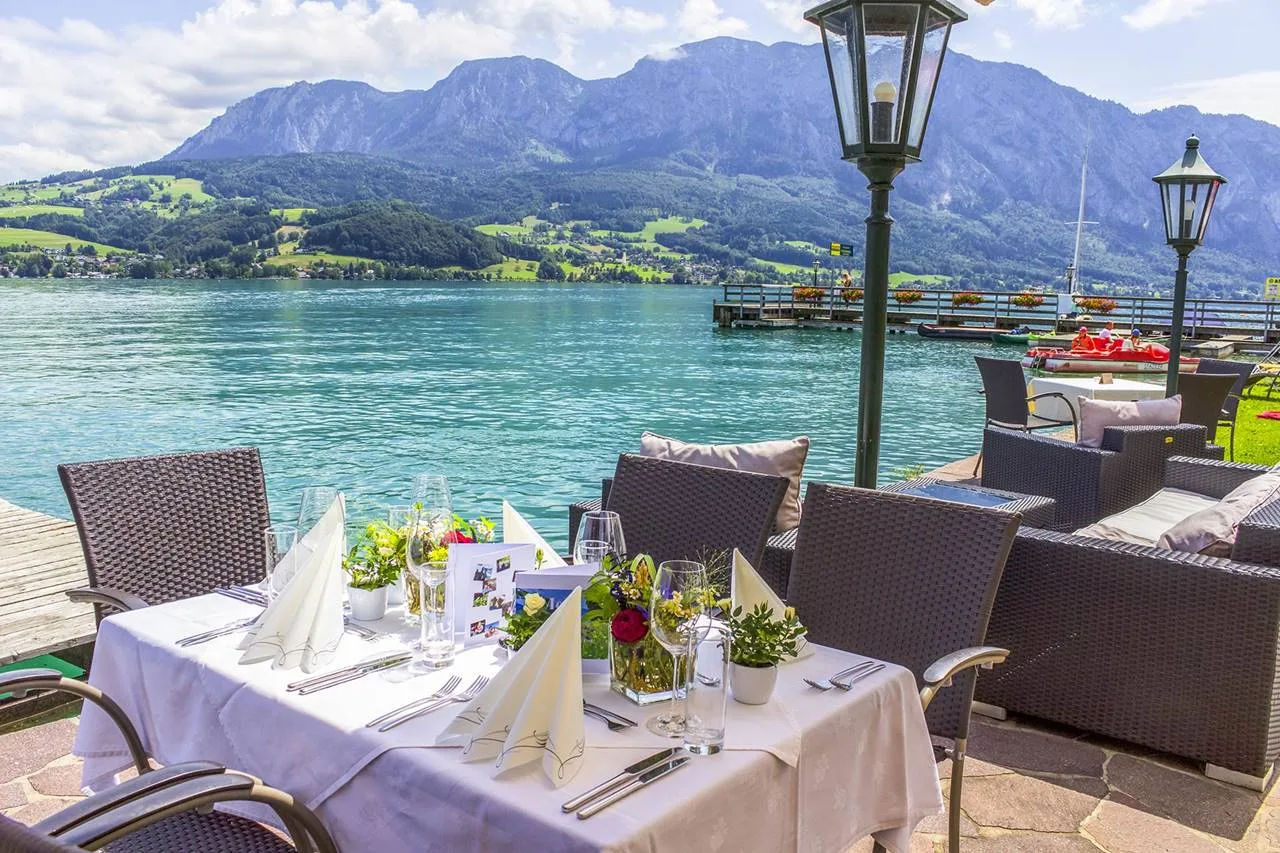 Representative hotel space: Outdoor dining tables overlook a lakeside promenade and mountain scenery.