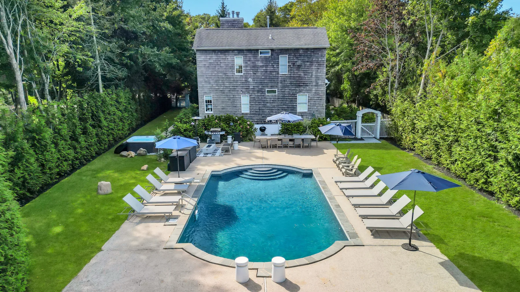 An outdoor swimming pool is surrounded by lounge seating and greenery.