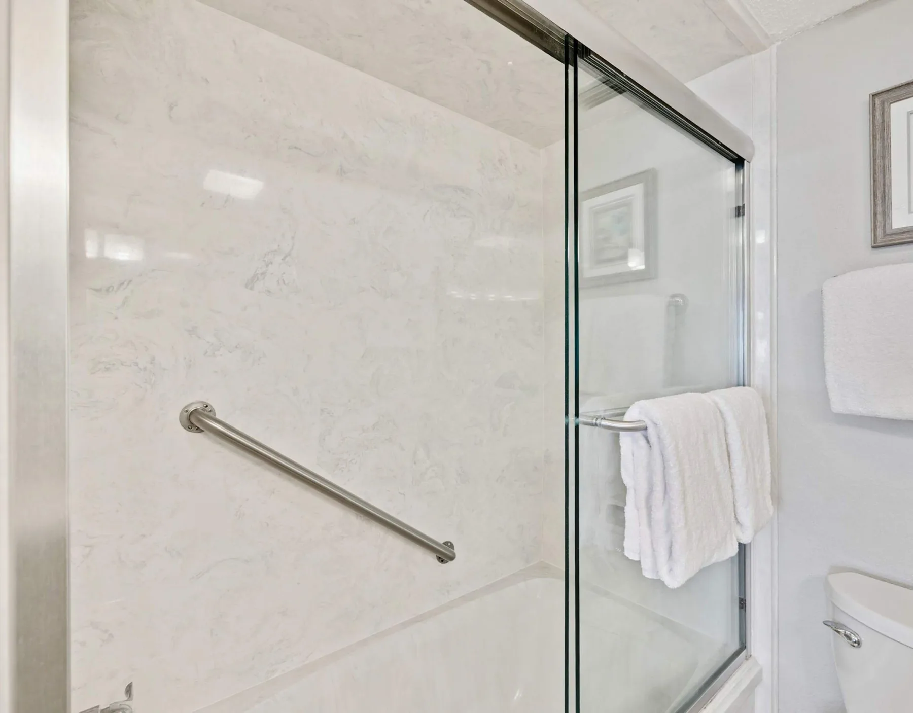 Una ducha de baño con un panel de vidrio y una barra de apoyo metálica.