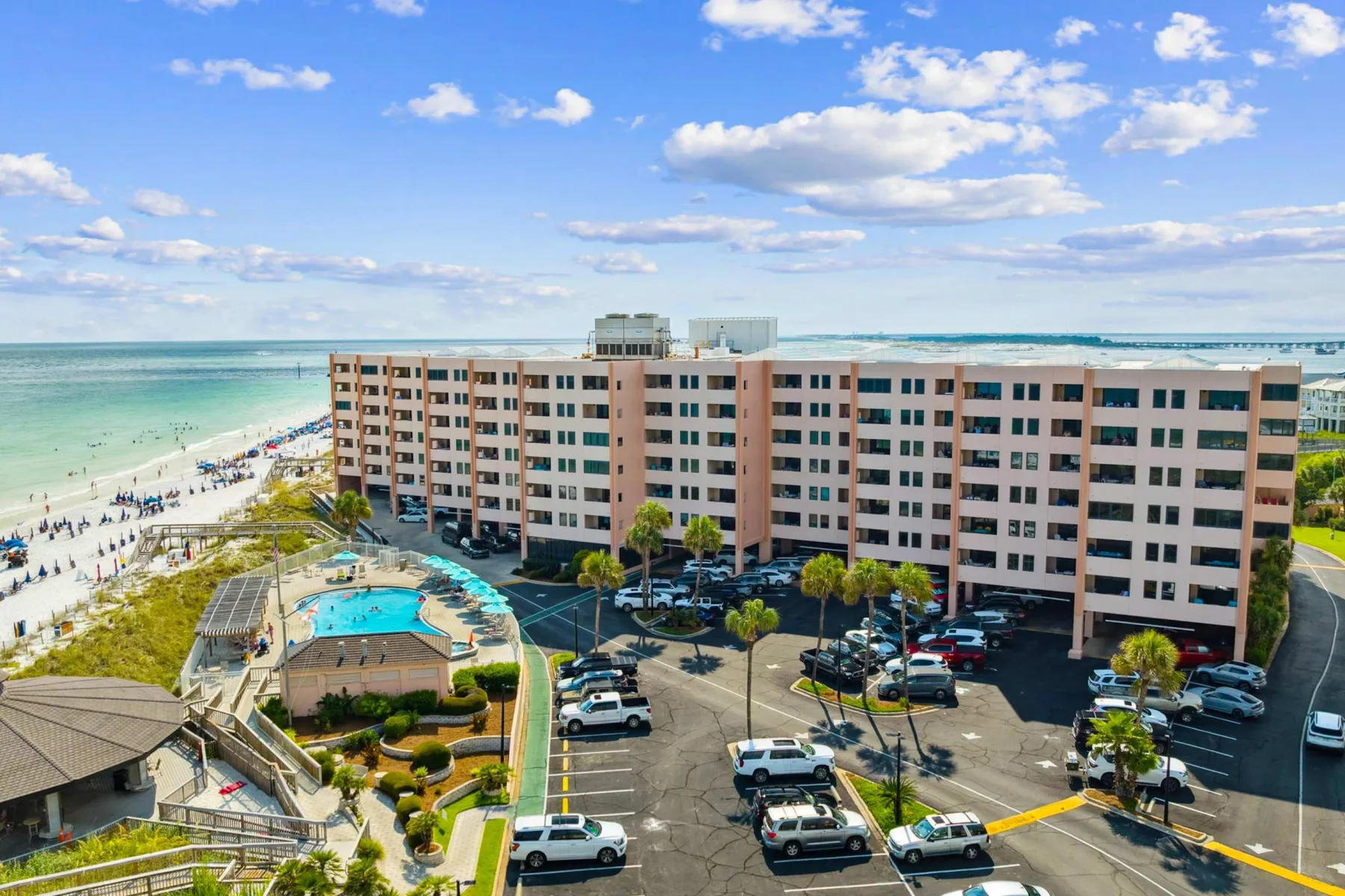 Zona común: Un edificio de apartamentos frente al mar, junto a una piscina y una zona de estacionamiento.