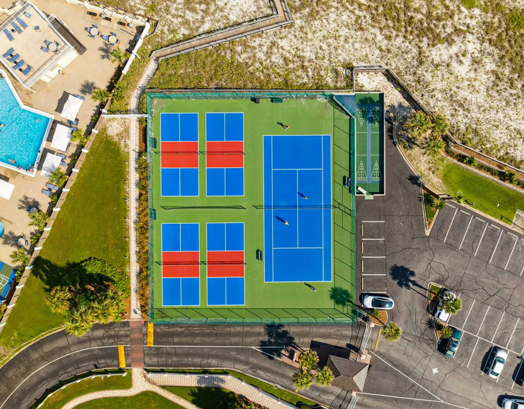 Zona común: Una vista aérea muestra varias canchas azules en un complejo deportivo verde junto a un estacionamiento.